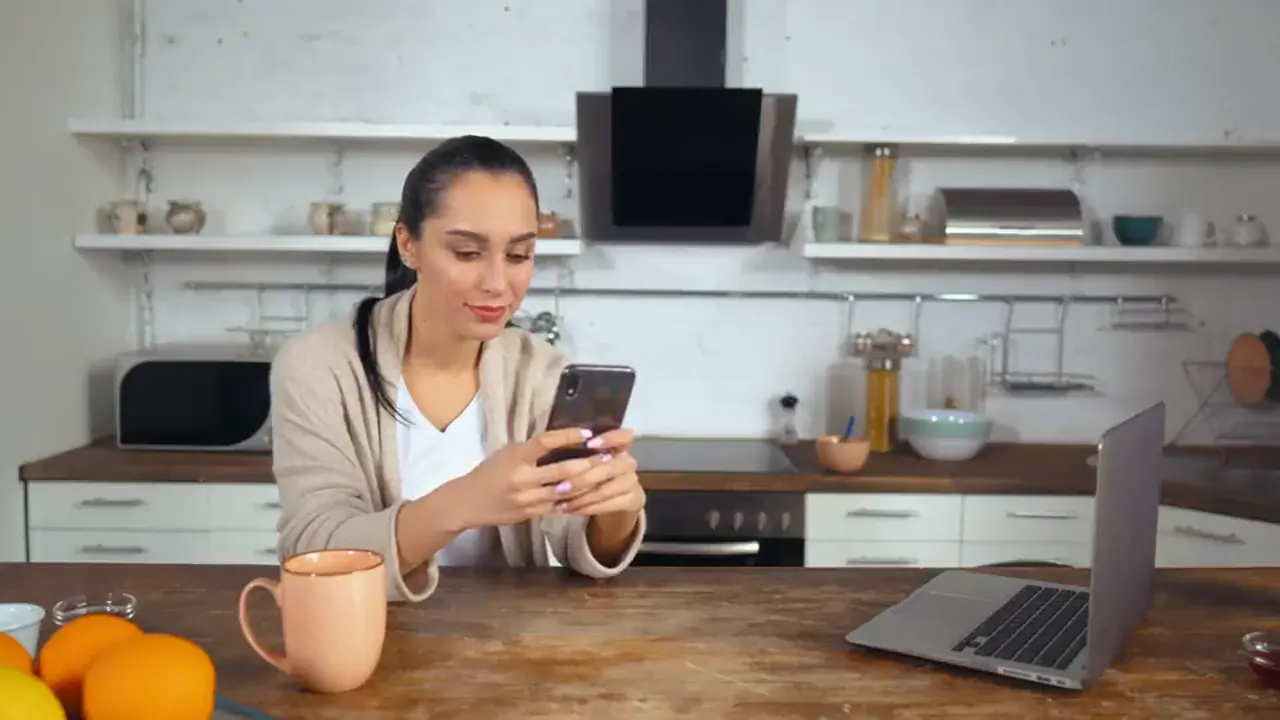 A woman at a kitchen table smiling at her phone