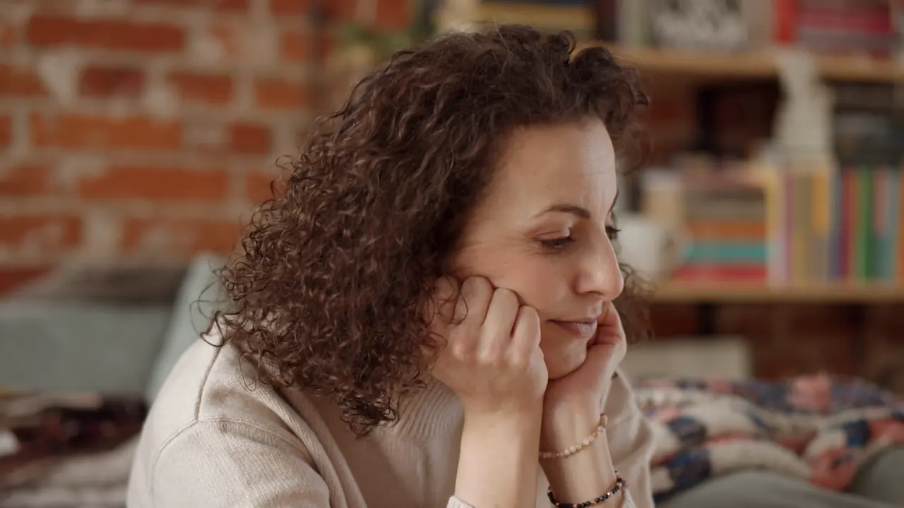 A woman at home, chin in her hands, looking down, lost in thought